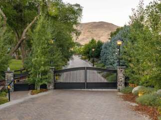 Welcome to this stunning estate, accessed through grand black iron gates and a paved driveway lined with mature trees and elegant lampposts.