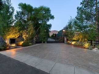 Welcome to this stunning estate, beautifully illuminated by landscape lighting that highlights the mature trees and elegant stone pillars.