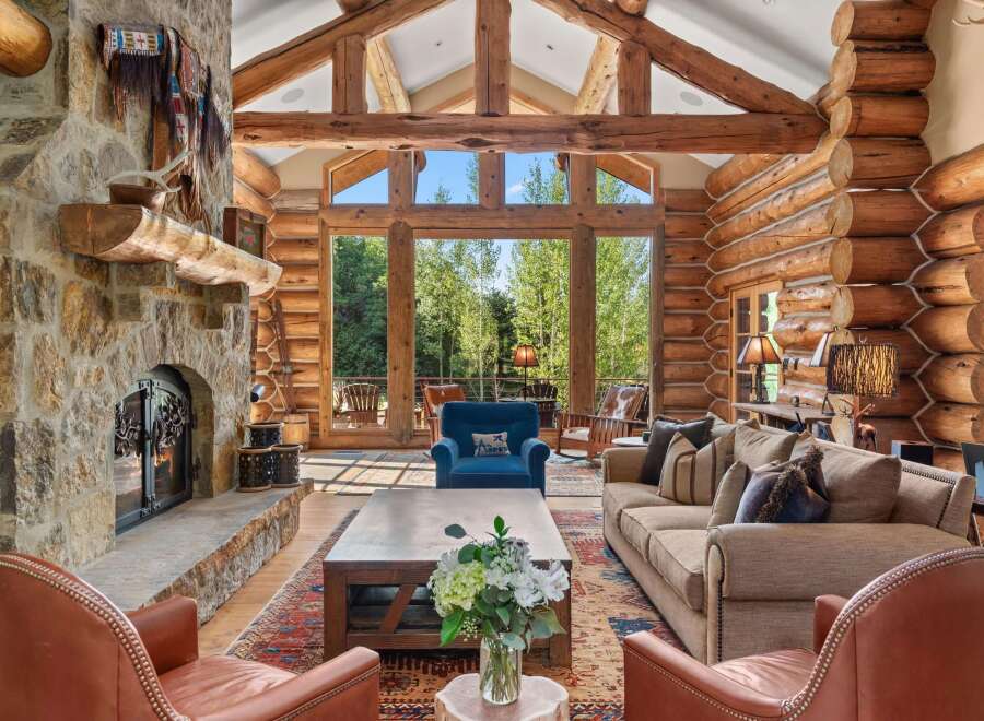 Experience rustic luxury in this stunning log cabin living room, featuring a grand stone fireplace and soaring vaulted ceilings with exposed wooden beams.