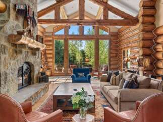 Experience rustic luxury in this stunning log cabin living room, featuring a grand stone fireplace and soaring vaulted ceilings with exposed wooden beams.