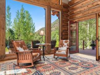 Experience rustic charm in this log cabin living area, featuring cozy rocking chairs with cowhide cushions and a large area rug.