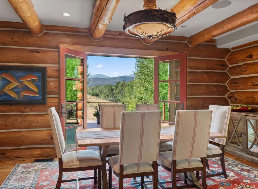 Experience rustic charm in this log cabin dining room, featuring a sturdy wooden table and chairs set against a backdrop of breathtaking mountain views.