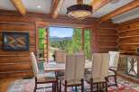 Experience rustic charm in this log cabin dining room, featuring a sturdy wooden table and chairs set against a backdrop of breathtaking mountain views.