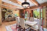Experience rustic elegance in this charming log cabin dining room, featuring a spacious wooden table set for six and a cozy seating area with a stone fireplace.
