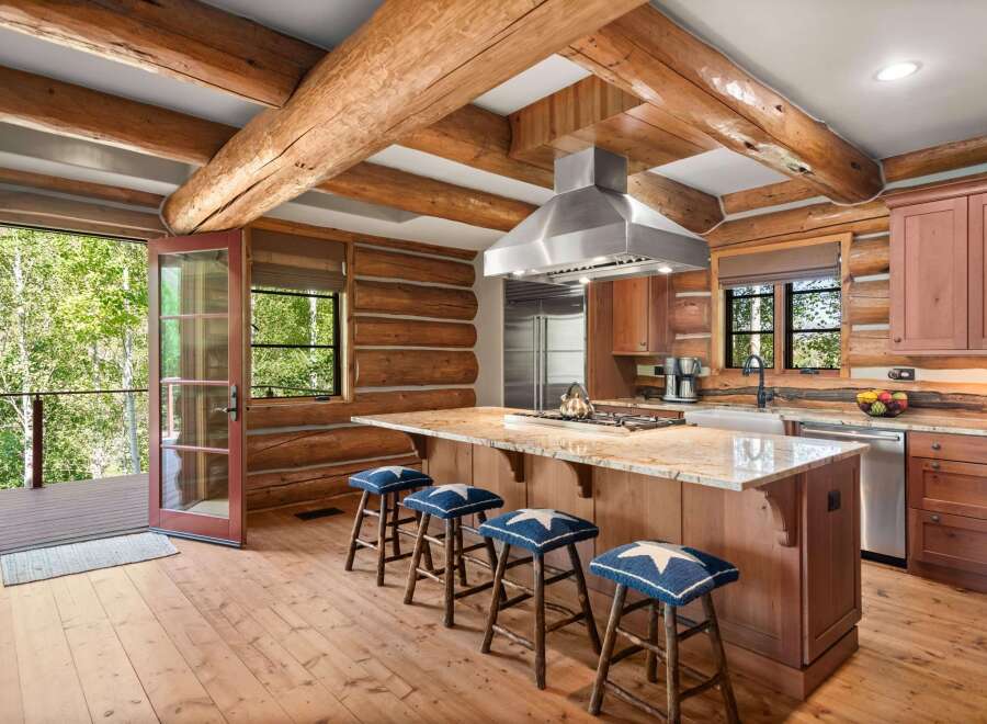 Experience rustic charm in this log cabin kitchen, featuring a large granite island with a gas stovetop and seating for four.