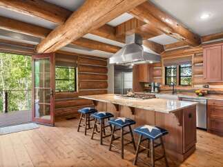 Experience rustic charm in this log cabin kitchen, featuring a large granite island with a gas stovetop and seating for four.