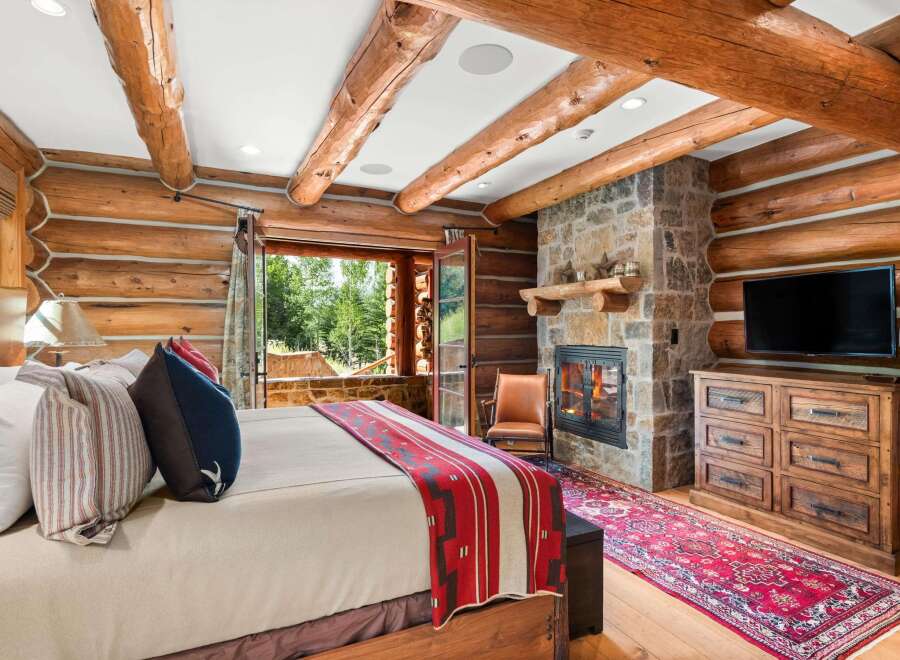 Experience rustic luxury in this charming log cabin bedroom, featuring a cozy fireplace and stunning mountain views.