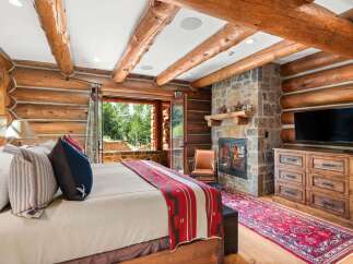 Experience rustic luxury in this charming log cabin bedroom, featuring a cozy fireplace and stunning mountain views.
