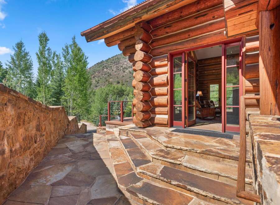 Experience rustic charm with this stunning log cabin, featuring a grand entrance with double doors and a stone pathway leading to the front porch.