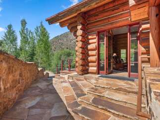 Experience rustic charm with this stunning log cabin, featuring a grand entrance with double doors and a stone pathway leading to the front porch.