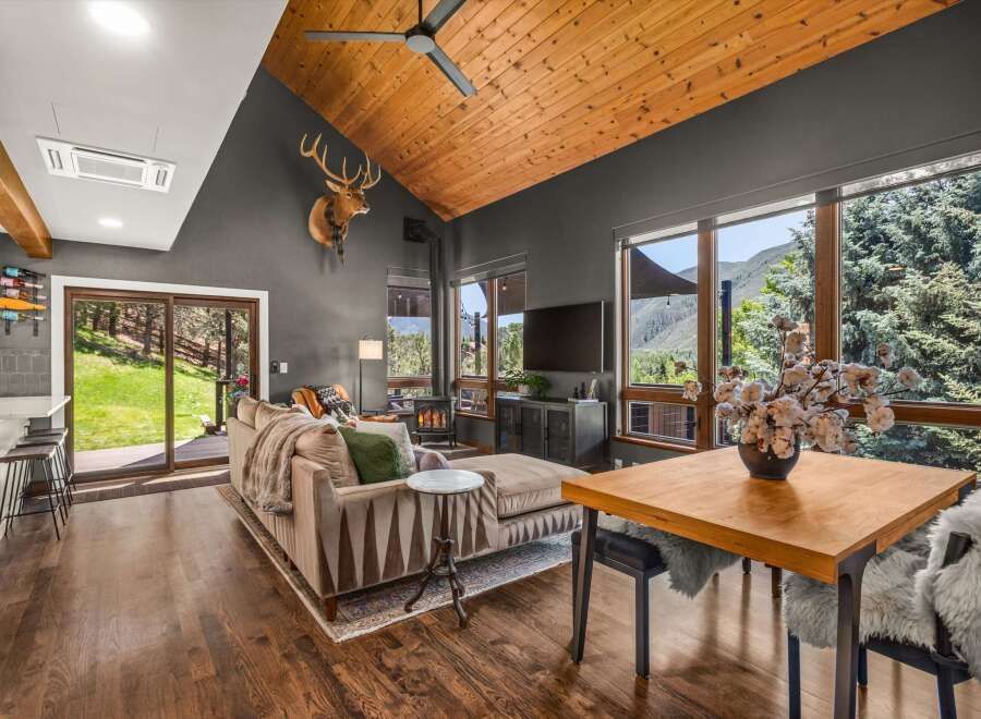 Experience breathtaking mountain views from this stunning living room, featuring a vaulted wood-paneled ceiling and a cozy fireplace.