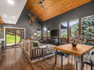 Experience breathtaking mountain views from this stunning living room, featuring a vaulted wood-paneled ceiling and a cozy fireplace.