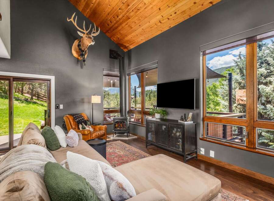 Experience rustic luxury in this stunning living room, featuring a vaulted wood-paneled ceiling and a majestic mounted elk.