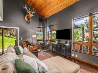 Experience rustic luxury in this stunning living room, featuring a vaulted wood-paneled ceiling and a majestic mounted elk.