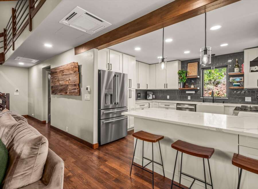 Experience modern living in this stunning kitchen featuring sleek white cabinetry, a spacious quartz island with bar seating, and a sophisticated dark tile backsplash.