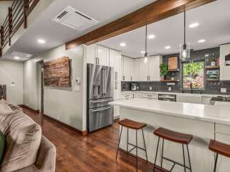 Experience modern living in this stunning kitchen featuring sleek white cabinetry, a spacious quartz island with bar seating, and a sophisticated dark tile backsplash.