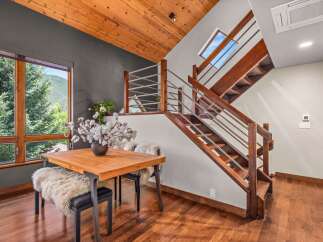 Experience modern mountain living in this stunning home featuring a sleek dining area with a wooden table and plush seating, complemented by large windows offering breathtaking views of the surrounding nature.