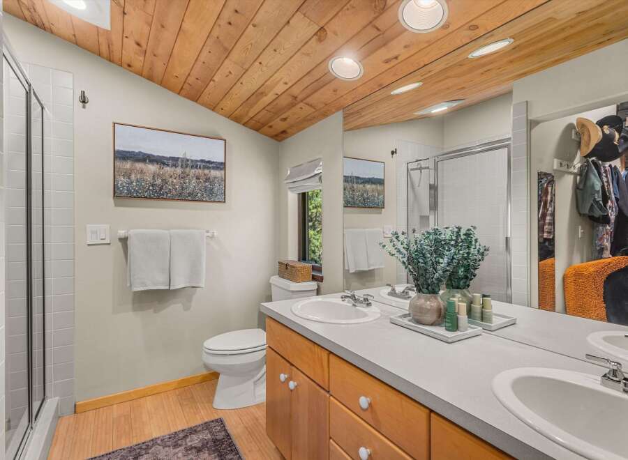 This beautifully appointed bathroom features a vaulted wood-paneled ceiling and a spacious vanity with dual sinks.
