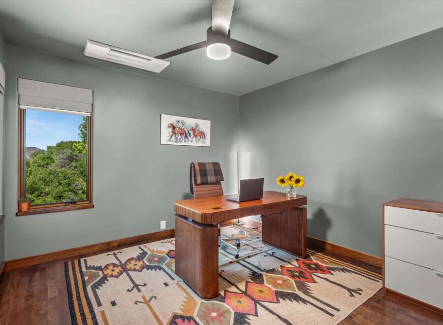 This home office features a stylish wooden desk with a laptop and a vase of sunflowers, complemented by a comfortable leather chair with a plaid throw.