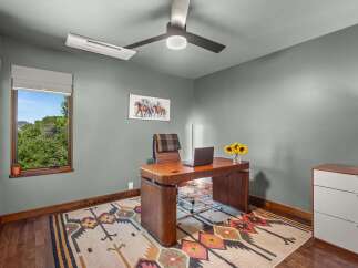 This home office features a stylish wooden desk with a laptop and a vase of sunflowers, complemented by a comfortable leather chair with a plaid throw.