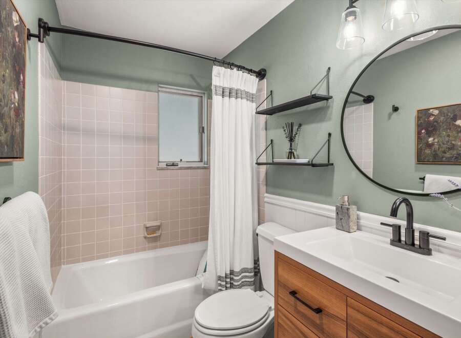 This modern bathroom features a sleek vanity with a wooden finish, complemented by a white countertop and a dark matte faucet.