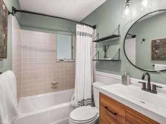 This modern bathroom features a sleek vanity with a wooden finish, complemented by a white countertop and a dark matte faucet.