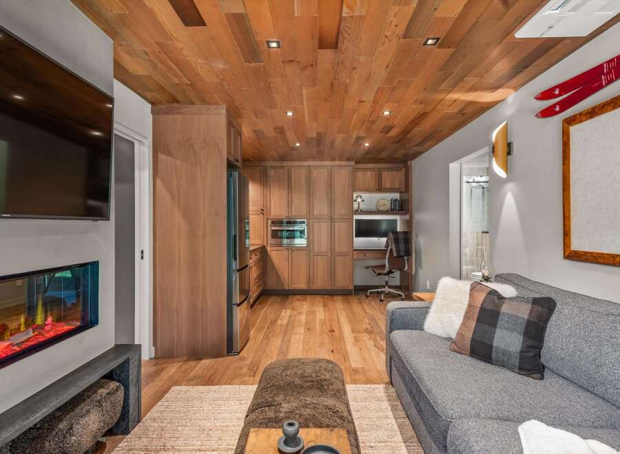Experience modern mountain living in this stunning space featuring a sleek fireplace and a beautifully paneled wood ceiling.