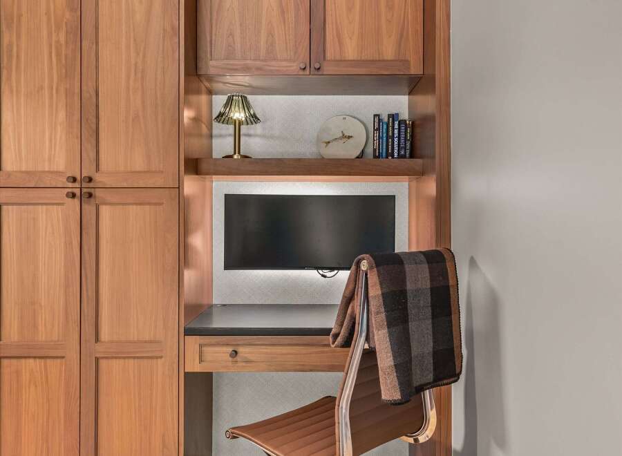 This home office features a built-in desk with a dark countertop and a single drawer, complemented by a comfortable brown leather office chair draped with a plaid blanket.