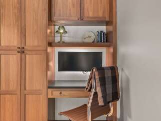 This home office features a built-in desk with a dark countertop and a single drawer, complemented by a comfortable brown leather office chair draped with a plaid blanket.