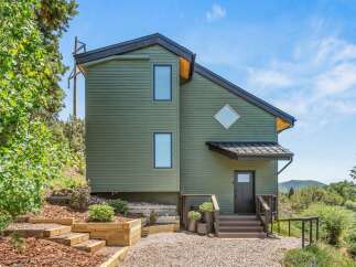 Discover this modern mountain home featuring a unique green exterior and a striking diamond-shaped window.