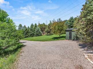Discover this charming property featuring a spacious gravel driveway leading to a lush green lawn and mature trees.