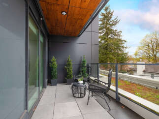 Enjoy your morning coffee on this modern balcony, featuring sleek black furniture and elegant potted evergreens.