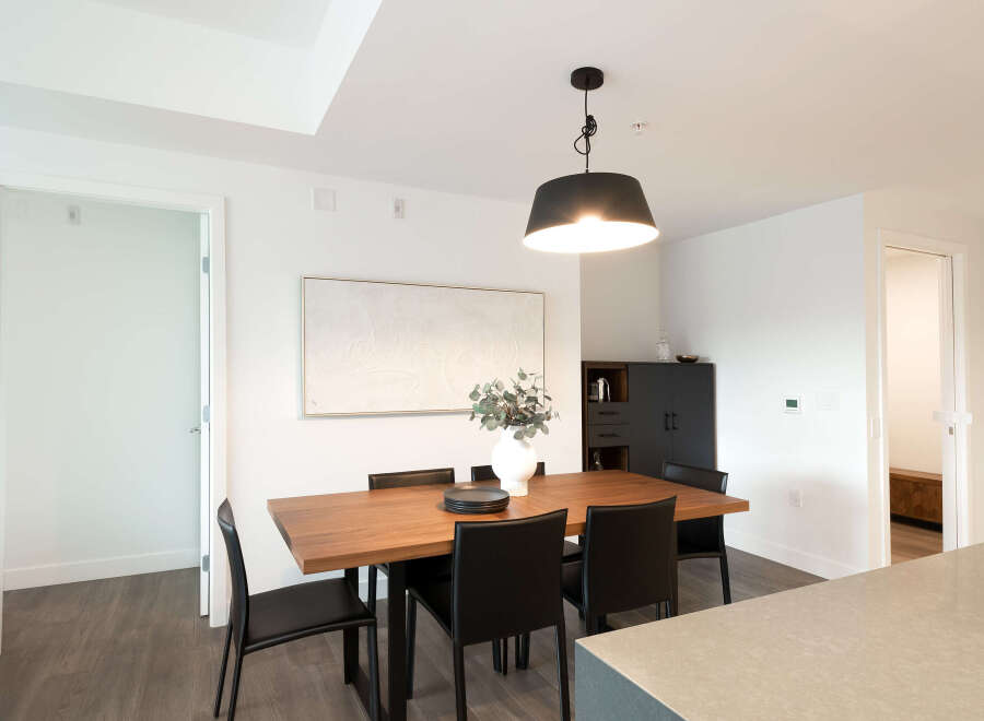 This modern dining room features a sleek wooden table with black chairs, illuminated by a stylish pendant light.
