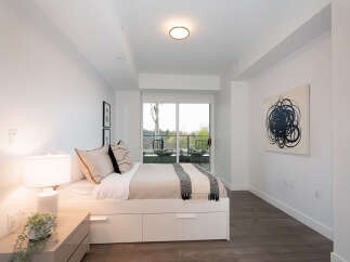 This modern bedroom features a comfortable queen-size bed with ample storage drawers, complemented by a stylish nightstand with a decorative lamp and a lush plant.