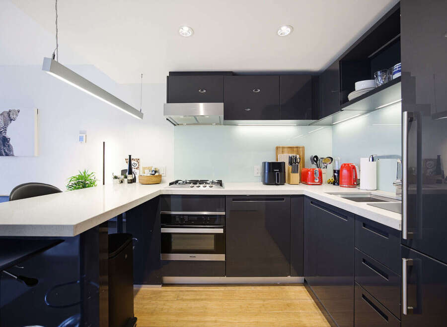 Experience modern living in this sleek, contemporary kitchen featuring high-gloss dark cabinetry and a spacious quartz countertop.