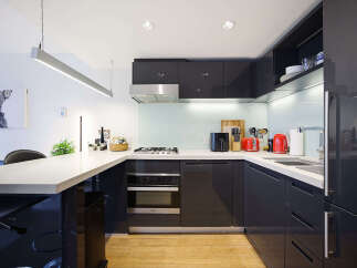 Experience modern living in this sleek, contemporary kitchen featuring high-gloss dark cabinetry and a spacious quartz countertop.