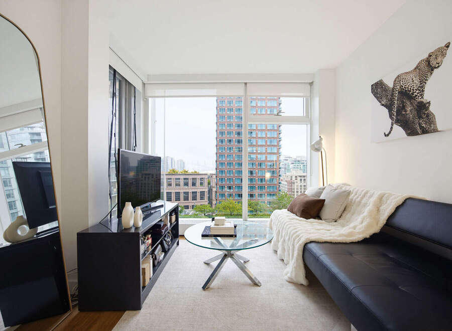 Experience modern city living in this stylish apartment featuring a sleek black sofa adorned with a cozy cream throw and accent pillows.