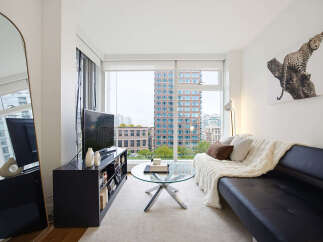 Experience modern city living in this stylish apartment featuring a sleek black sofa adorned with a cozy cream throw and accent pillows.