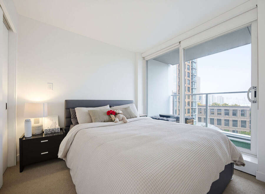 Experience urban living in this bright and airy bedroom, featuring a comfortable queen-size bed and a large sliding glass door that opens to a private balcony with city views.