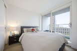 Experience urban living in this bright and airy bedroom, featuring a comfortable queen-size bed and a large sliding glass door that opens to a private balcony with city views.