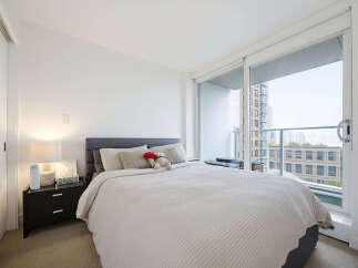 Experience urban living in this bright and airy bedroom, featuring a comfortable queen-size bed and a large sliding glass door that opens to a private balcony with city views.