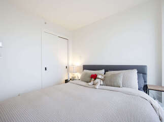 Experience modern comfort in this beautifully appointed bedroom, featuring a plush king-sized bed adorned with decorative pillows and a charming teddy bear.
