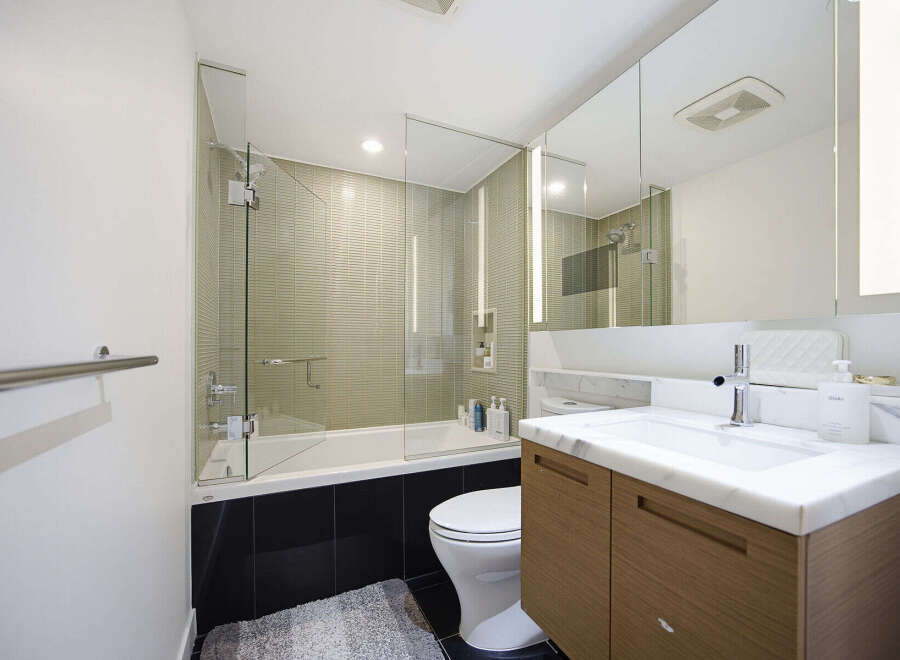 This modern bathroom features a sleek glass-enclosed bathtub and shower area with textured tile walls.