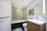This modern bathroom features a sleek glass-enclosed bathtub and shower area with textured tile walls.