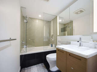 This modern bathroom features a sleek glass-enclosed bathtub and shower area with textured tile walls.