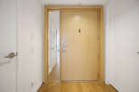Step into a welcoming entryway featuring a sleek, light wood front door with a modern handle and peephole.