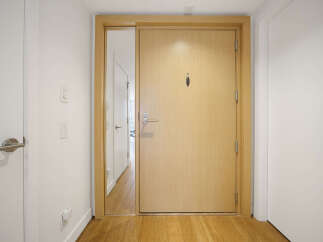 Step into a welcoming entryway featuring a sleek, light wood front door with a modern handle and peephole.