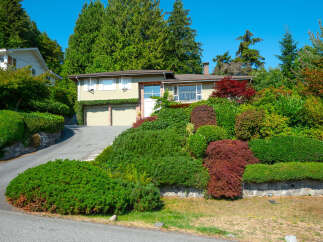 This charming home features a beautifully landscaped hillside with a variety of lush greenery and mature trees, creating a private and serene atmosphere.