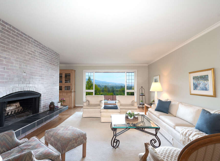 Experience breathtaking panoramic views from this stunning living room, featuring a cozy brick fireplace and ample natural light pouring in through large windows.
