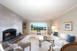 Experience breathtaking panoramic views from this stunning living room, featuring a cozy brick fireplace and ample natural light pouring in through large windows.